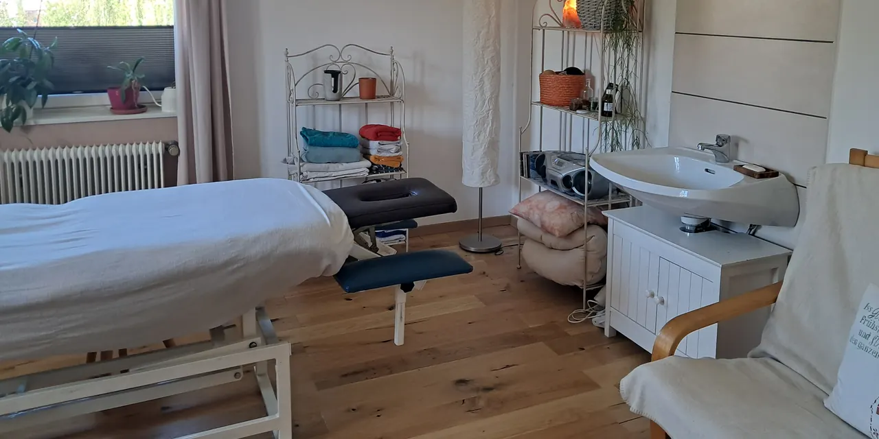 Heller Behandlungsraum mit Massageliege am großen Fenster