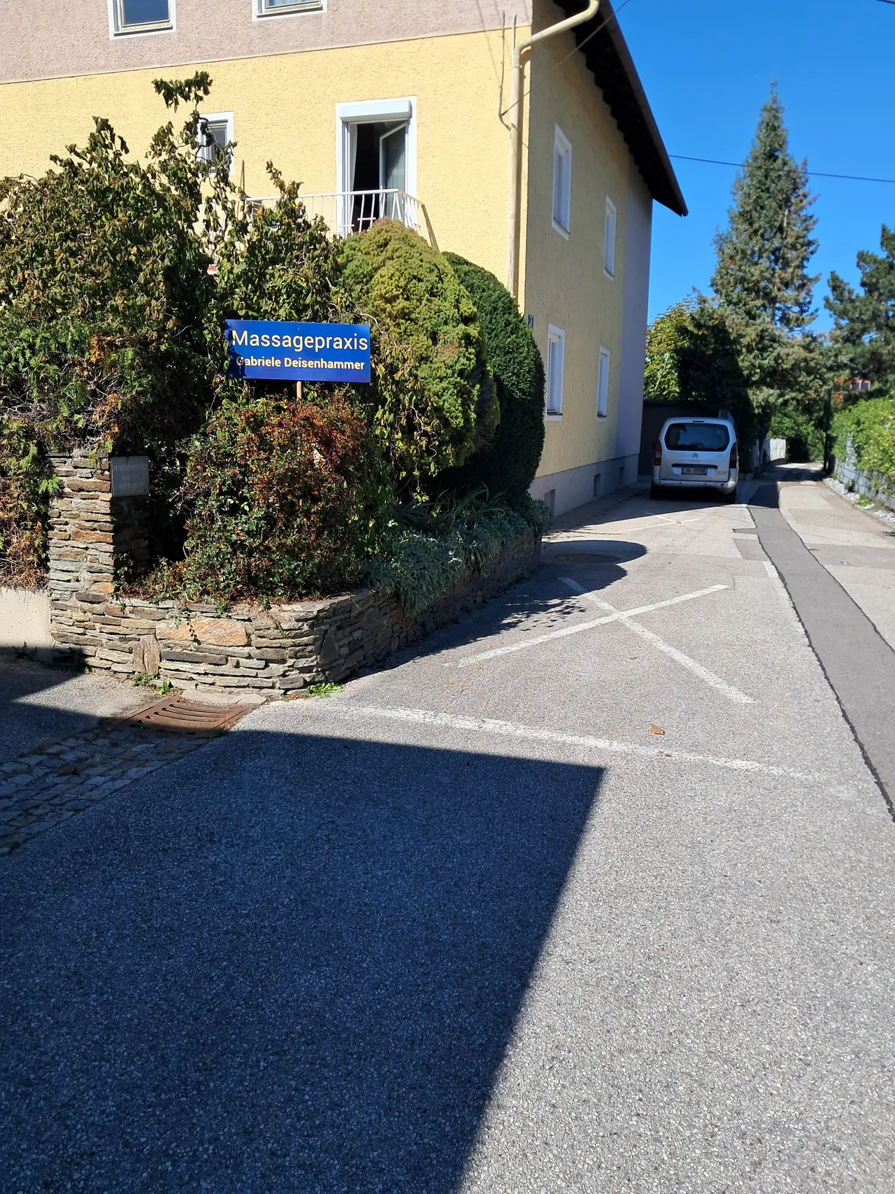 Straßenansicht der Praxis mit Praxisschild und Kundenparkplatz direkt vor dem Haus