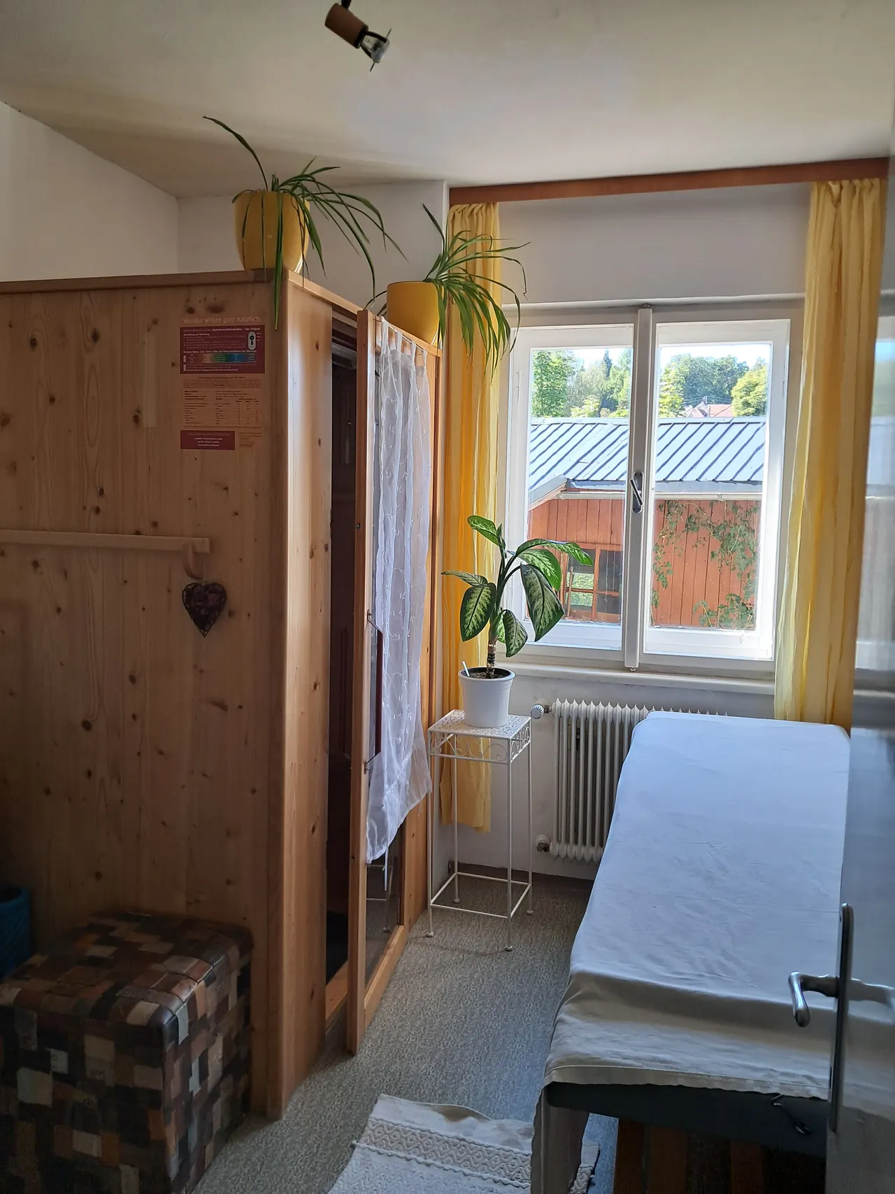 Raum mit der hölzernen Infrarotkammer und Liege am Fenster